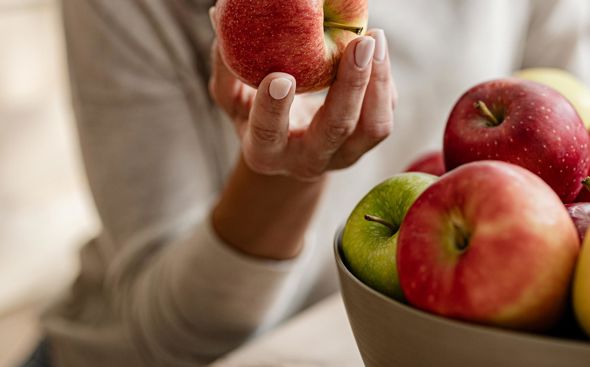 Donna tiene una mela rossa in mano e osserva una ciotola con altre mele fresche
