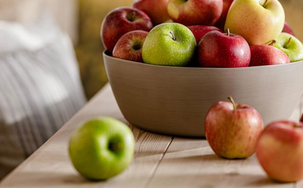 Ciotola con mele fresche assortite su tavolo in legno, montagne visibili dietro