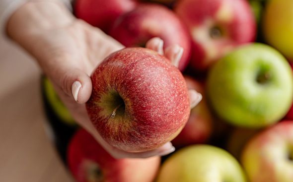 Primo piano di una mela rossa tenuta in mano, sfondo sfocato con cesto di mele fresche