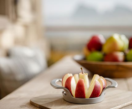 Mela tagliata su tagliere di legno in primo piano, ciotola con mele assortite e montagne sullo sfondo